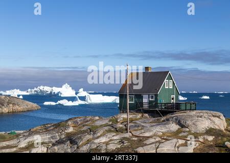 Qeqertarsuaq, Grönland, 5. Juli 2018: Ein grünes Holzhaus mit Eisbergen im Hintergrund Stockfoto