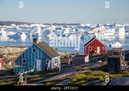 Rodebay, Grönland, 09. Juli 2018: Bunte Holzhäuser mit Eisbergen im Hintergrund. Rodebay, auch bekannt als Oqaatsut, ist eine Fischersiedlung Stockfoto