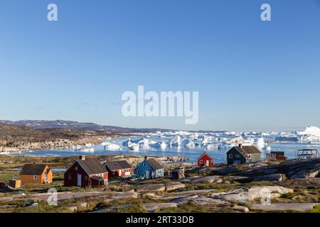 Rodebay, Grönland, 09. Juli 2018: Bunte Holzhäuser mit Eisbergen im Hintergrund. Rodebay, auch bekannt als Oqaatsut, ist eine Fischersiedlung Stockfoto