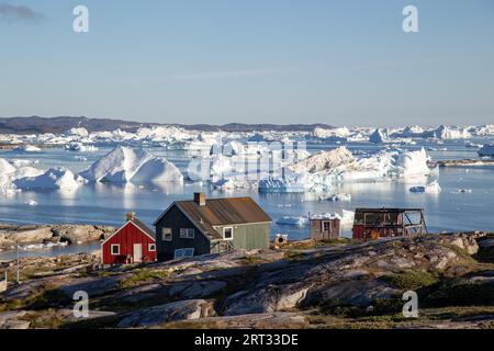 Rodebay, Grönland, 09. Juli 2018: Bunte Holzhäuser mit Eisbergen im Hintergrund. Rodebay, auch bekannt als Oqaatsut, ist eine Fischersiedlung Stockfoto