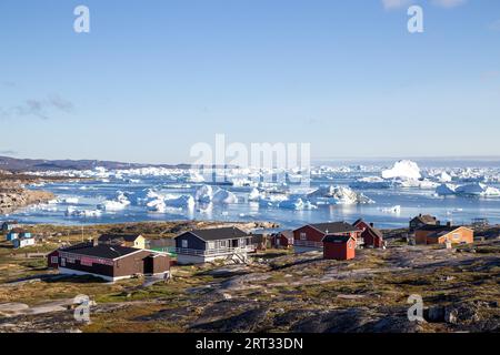 Rodebay, Grönland, 09. Juli 2018: Bunte Holzhäuser mit Eisbergen im Hintergrund. Rodebay, auch bekannt als Oqaatsut, ist eine Fischersiedlung Stockfoto