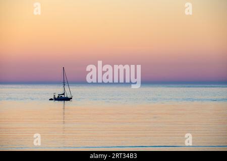 Eine Yacht vor Anker bei Sonnenuntergang an der Nordküste von Anglesey bei Cemaes in Wales Stockfoto