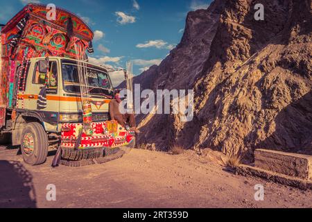 Karakoram Highway, Pakistan, 19. Juli 2018: Pakistanischer Mann reist auf der vorderen Stoßstange eines dekorierten Lkws auf einer gefährlichen Bergstraße. Anschaulich Stockfoto