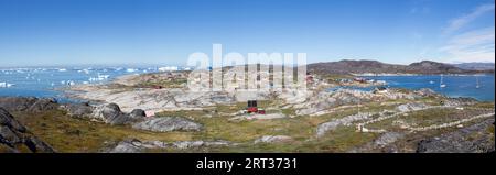 Rodebay, Grönland, 09. Juli 2018: Bunte Holzhäuser mit Eisbergen im Hintergrund. Rodebay, auch bekannt als Oqaatsut, ist eine Fischersiedlung Stockfoto