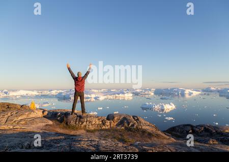 Ilulissat, Grönland, 7. Juli 2018: Junger Mann, der den Ilulissat Icefjord in der Mitternachtssonne betrachtet. Ilulissat Icefjord wurde zum UNESCO-Weltkulturerbe erklärt Stockfoto