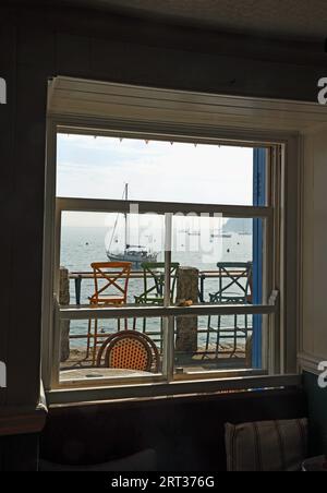 Blick auf Cawsand Bay durch ein Pub-Fenster auf dem Cleeve in Kingsand Cornwall. Aufrechter allgemeiner Eindruck einer Kneipe am Wasser mit Stühlen und Booten und Kopfenden Stockfoto