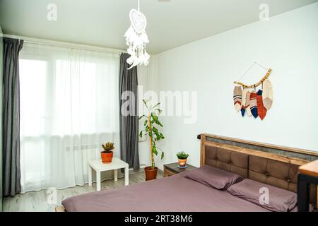 Modernes Schlafzimmer mit Elementen im Boho-Stil. Großes Bett, Nachttische und Makramee-Platten an der Wand. Stockfoto