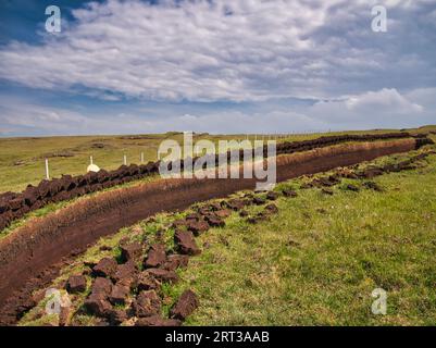 Frisch geschnittene Torfblöcke, die sich in Reihen über einem Graben in der Torfbasis stapeln und in der Sonne liegen, um zu trocknen. Aufgenommen in den Äußeren Hebriden, Schottland, Großbritannien auf A Stockfoto