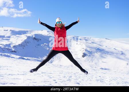 Fröhliche Frau in warmer Kleidung, die in der Luft auf Schneelandschaft springt Stockfoto
