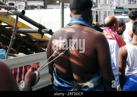 London, Großbritannien. September 2023. Tausende hinduistische Gläubige versammeln sich in Walthamstow im Osten Londons, um die jährliche Prozession des Sri Karphaha Vinayagar Temple Rathayatra zu feiern, bei der ein Wagen von Gläubigen in einem Zeichen der Einheit und des Glaubens gezogen wird. Einige Devotees entscheiden sich dafür, dass Haken durch ihren Rücken gepierct werden, die an Seilen befestigt sind, die andere Devotees halten, und ein Devotee auf der Prozession wird von ihren hinteren Haken auf eine Struktur auf einem Van gehisst, wo er für die Dauer des Tages gehängt wird. © Simon King/Alamy Live News Stockfoto