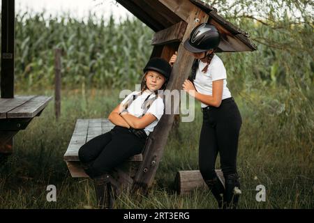 Porträt von Mädchen Jockeys, einer sitzt auf einer Bank, der zweite steht in der Nähe. Stockfoto