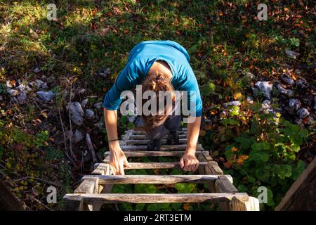 Erwachsene Frau mit blauem Sweatshirt klettert eine Holzleiter hinauf Stockfoto