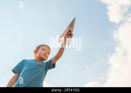 Der kleine Junge feuert ein Papierflugzeug in die Luft. Kind startet eine Papierebene Stockfoto