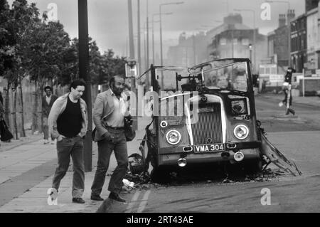 Toxteth stößt in den 1980er Jahren auf Großbritannien auf. Am Morgen nach der Nacht der Unruhen laufen zwei Männer an einem ausgebrannten und zerstörten Bus oder Van vorbei. Toxteth, Liverpool, England um Juli 1981. HOMER SYKES Stockfoto