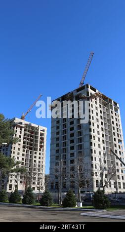 Mehrfamilienhäuser im Bau mit Turmdrehkranen vor blauem Himmel, vertikales Bild, neue städtische Infrastruktur im Prozess Stockfoto