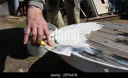 Der Master wendet eine elastische Lösung mit einem schmalen Spatel auf eine runde Netzoberfläche an, wodurch einzigartige Möbel aus verschiedenen Materialien entstehen Stockfoto