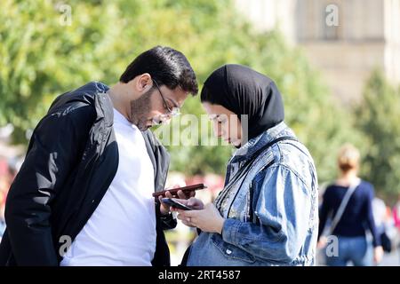 Paar mit Smartphones, die im Herbst auf einer Straße in der Stadt stehen Stockfoto