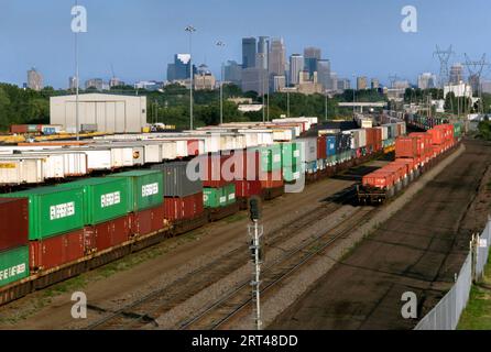 BNSF-Eisenbahnwaggons mit Doppelstapel, beladen mit intermodalen Transportcontainern in St. Paul, Minnesota. Die Skyline von Minneapolis im Hintergrund. Stockfoto