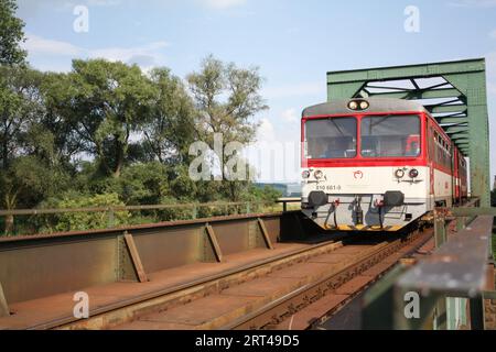 Ein Dieselzug, der auf einer eingleisigen Eisenbahnbrücke in Komárany, Slowakei, vorbeifährt. Stockfoto