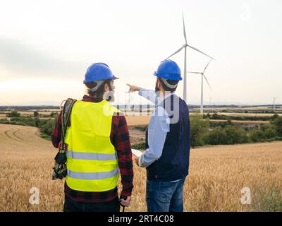 Zwei technische Mitarbeiter mit dem Rücken drehten sich um und zeigten auf ein Feld von Windkraftanlagen. Erneuerbare Energien Stockfoto