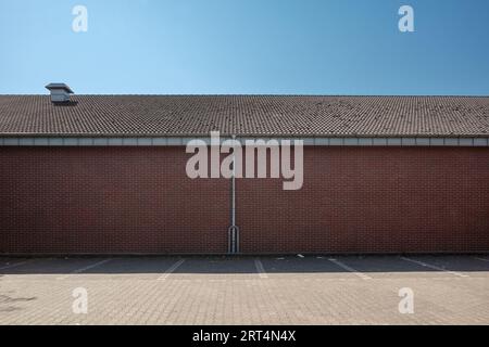 Außenansicht des leeren Parkplatzes und Hintergrund von Ziegelwänden, Metallregenrinne und Dach vor blauem Himmel. Stockfoto