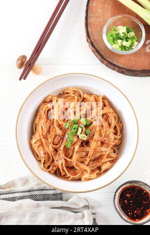 Chinesische Reisnudel mit Chiliöl und gehackter grüner Zwiebelauflage. Serviert auf weißer Schüssel, weißer Tisch Stockfoto