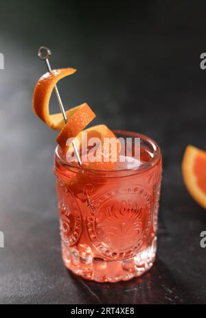 Klassischer Negroni-Cocktail aus Retro-Glas mit Eis- und Orangenschale auf schwarzem Tischhintergrund Stockfoto