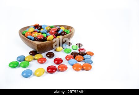 Stapel bunte Schokoladenbonbons in herzförmiger Holzschale isoliert auf weißem Hintergrund, Draufsicht Stockfoto