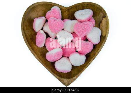 Ein Haufen herzförmiger Zuckerbonbons auf einer herzförmigen Holzschale auf weißem Hintergrund Stockfoto