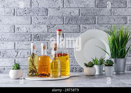 Verschiedene Ölsorten in stilvollen Glasflaschen auf der Marmorarbeitsplatte der Küche vor der grauen Backsteinwand. Küchenhintergrund Stockfoto