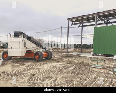 Baustelle eines Industriekomplexes. Maschine für den Transport schwerer Baumaterialien in Orange. Schmutz auf dem Boden, Spuren schwerer Maschinen Stockfoto