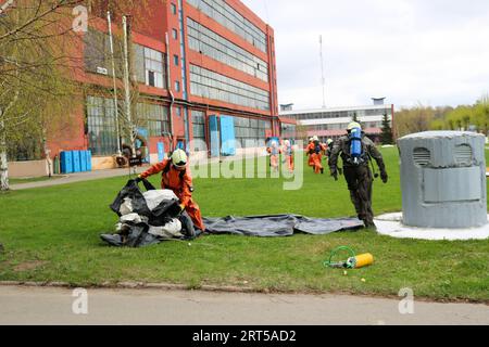 Professionelle Feuerwehrleute, Rettungskräfte in feuerfesten Schutzanzügen, Helme und Gasmasken fliehen aus einem Industriegebäude in einer Ölraffinerie, p Stockfoto