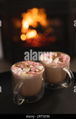 Nahaufnahme von zwei Tassen heißer Schokolade mit Marshmallows und offenem Feuer im Kamin, Kopierraum Stockfoto