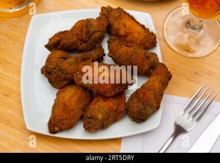 Gebratene Hähnchenflügel in Brotkrumen auf quadratischem weißem Teller Stockfoto