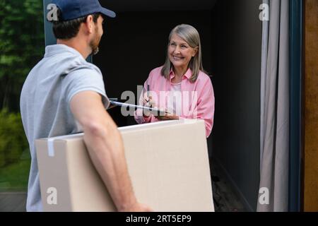 Die Frau nimmt die Lieferung von Kisten vom Lieferer an. Stockfoto