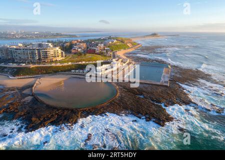 Weitwinkelblick auf Newcastle Ocean Baths und Canoe Pool bei Sonnenaufgang in Newcastle mit Blick auf Nobbys Lighthouse. Stockfoto