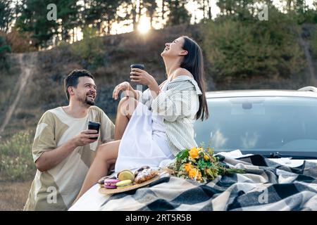 Ein Paar genießt Picknick-Zeit bei Sonnenuntergang auf einer Wiese, die in der Nähe des suv-Autos steht. Stockfoto