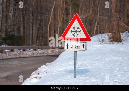 Vorsicht vor Eis oder Schnee, dreieckiges Warnschild an der Straße im Winter, selektiver Fokus Stockfoto