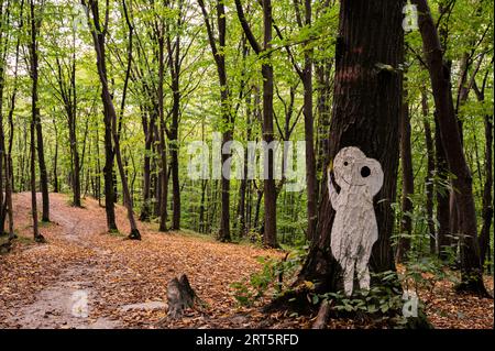 Weiße halloween-Silhuette von Mann oder Außerirdischer auf Baum im Wald abgebildet, bedeckt mit gelben trockenen Blättern, mit einer anderen solchen Silhuette auf Hintergrund. Sceni Stockfoto