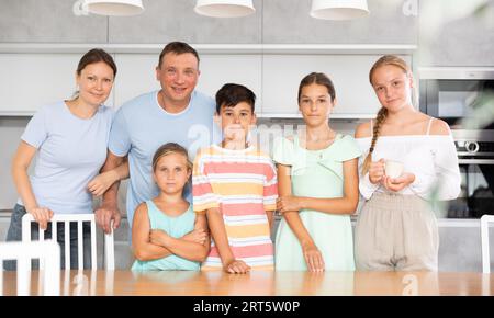 Glücklicher Vater und Mutter mit drei Töchtern und Sohn stehen neben dem Küchentisch. Stockfoto