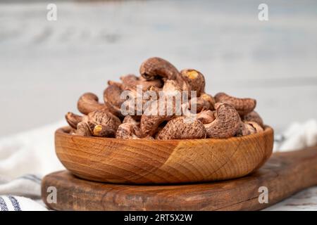 Cashewkerne mit Schale in Holzschale. Cashew auf weißem Holzgrund Stockfoto