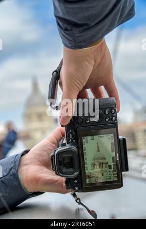 LONDON - 24. April 2023: Nahaufnahme der Hände mit einer Kamera, die einen einzigartigen Blick auf die St Paul's Cathedral auf der Rückwand der Kamera aufnehmen. Stockfoto