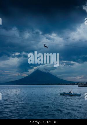 Mann auf Seilrutsche über der Bucht von Legazpi City mit Mayon Vulkan. Stockfoto