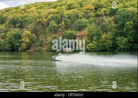 Zwei Personen, die Jet-Ski auf dem Fluss mit wunderschönen grünen Bäumen im Hintergrund reiten. Geschwindigkeit, Sport, Urlaub, extrem Stockfoto