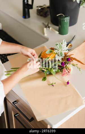 Eine Frau, die einen Strauß Herbstblumen in ihrer Küche zusammenbindet Stockfoto