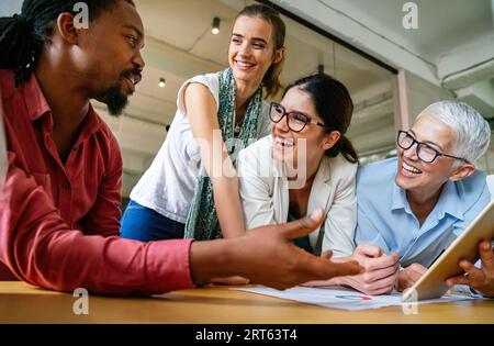 Lächelnd treffen sich verschiedene Kollegen in einem Brainstorming in der Vorstandsetage, um gemeinsam Finanzstatistiken zu diskutieren Stockfoto