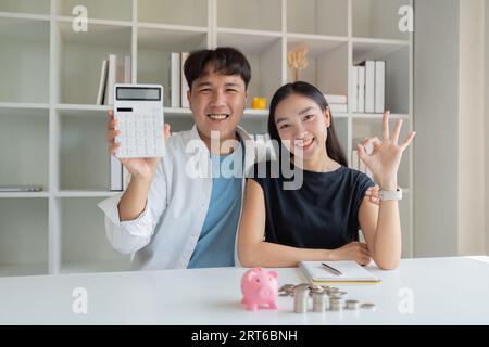 Junge Paare, die sich in Investitionen sicher sind, finanzielle Planung zusammen, Frau zeigt OK Zeichen Mann zeigt Taschenrechner Stockfoto