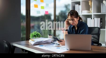 Überarbeitete Geschäftsfrau Finanzierin, während sie im Büro an Notebooks und Tablets arbeitet Stockfoto