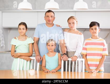 Glücklicher Vater mit drei Töchtern und Sohn steht neben dem Küchentisch. Stockfoto