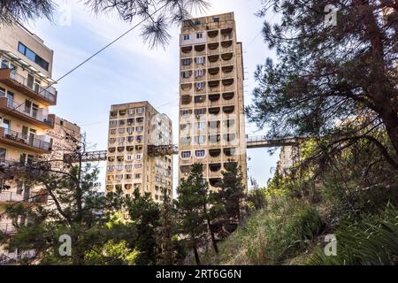 Der Wohnkomplex Tbilisi Skybridge (Nutsubidze Skybridge) in der Ermile-Bedia-Straße in Tbilissi, Georgien, erhebt sich mit zwei Turmblöcken über einem bewaldeten Hang. Stahlgänge verbinden die Türme mit ihren Nachbargebäuden in schwindelerregender Höhe. Die Fassaden zeigen hufeisenförmige Fensteröffnungen. Links steht ein Wohnhaus mit Balkonen, davor befinden sich Kiefern und Gräser. Der Komplex verbindet die Stadtteile Saburtalo und Nutsubidze am Hang. Er liegt etwa 11 Kilometer vom historischen Stadtzentrum entfernt. Die Architekten Otar Kalandarishvili und Gaioz Potskhishvili entwarfen ihn Stockfoto